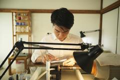 A man in a white shirt meticulously engraves a glass in a well-lit workshop.