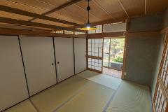 A Japanese room with tatami mats, shoji doors, and a view of a garden. The room has a modern light fixture and a ceiling-mounted air conditioner.