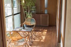 A cozy sunlit nook with woven chairs around a small table, featuring a book and mug, situated next to a window and cabinet, creating a peaceful indoor setting.